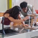 2 élèves font une manipulation en cours de sciences physiques. Le visage de l'élève de face est pixelisé.