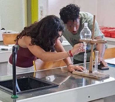 2 élèves font une manipulation en cours de sciences physiques. Le visage de l'élève de face est pixelisé.